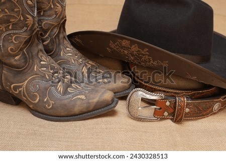 embroidered brown boots, dark brown hat and belt with silver buckle - text space on bottom - beige background - cowgirl style for country line dance Royalty-Free Stock Photo #2430328513