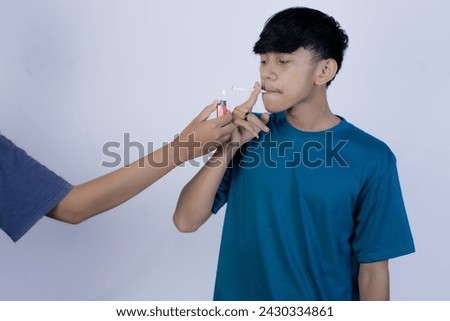 Young Asian man with a cigarette in his mouth and the help of his friend lighting his cigarette, isolated in the gray background.
