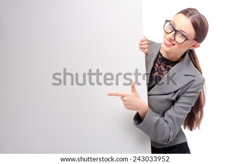 Happy smiling young business woman wearing glasses showing blank signboard pointing with her finger, isolated on white background