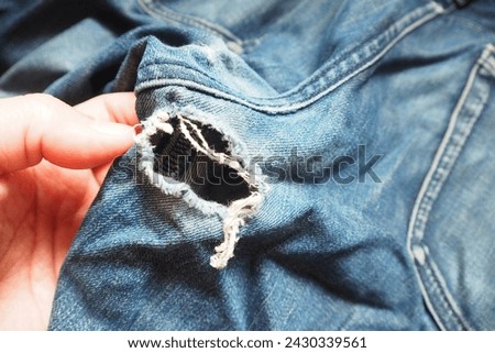 Hand touching ripped dark blue jeans cracked with hole at the crotch near back pocket Need to repair by sewing machine and stitching Royalty-Free Stock Photo #2430339561