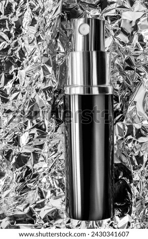 Perfume spray atomizer against crumpled silver foil background