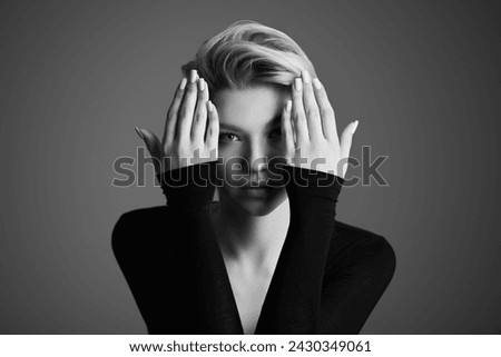 Art black-and-white portrait of a graceful young blonde woman with a short haircut, posing expressively in black bodysuit. Dark gray studio background with copy space. Female beauty. Royalty-Free Stock Photo #2430349061