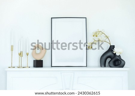 Stylish room decorated with vase with orchids flowers, vintage metal candlesticks with candles, picture on fireplace shelf. White modern decorated mantel in interior design Scandinavian living room. 