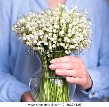 A young woman holds a vase with lilies of the valley. Spring mood. Close-up. Selective focus.
