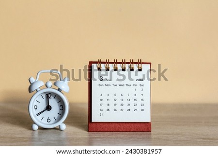 Monthly desk calendar for March 2024 and clock on a wooden table.