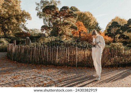 Beautiful young woman takes photos with a professional camera in autumn forest. Smiling girl enjoying autumn weather. Rest, relaxation, lifestyle concept. Young photographer takes pictures of autumn
