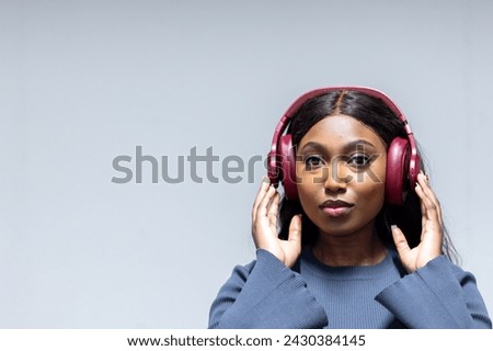 The image features an African American woman enjoying a moment of music, as evidenced by the crimson headphones she wears. She holds them gently with both hands, and her eyes are softly directed