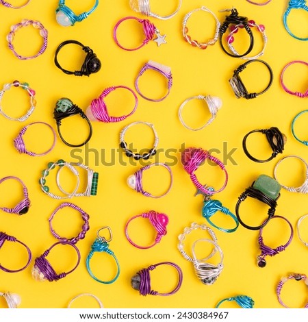 Handmade rings made of wire and natural stones scattered on a yellow background. 