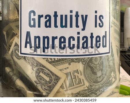 Dollar bills in a transparent glass tip jar with sign, "Gratuity is Appreciated," at a tiki bar in southwest Florida