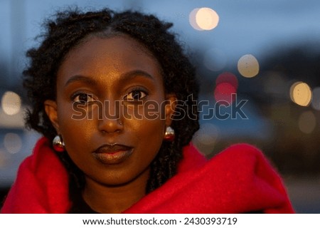 This portrait captivates with a young woman's direct stare into the lens, her face illuminated by the gentle dusk light. The red scarf is a vibrant contrast to the twilight, draped around her for