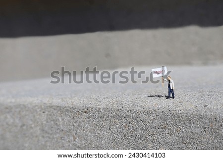 Tiny Man on Sidewalk Holds Sign Demanding More.