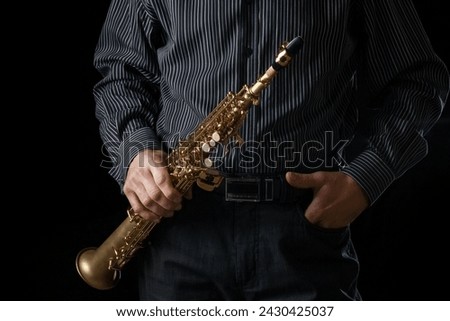 soprano saxophone in the hands of a guy on a black background Royalty-Free Stock Photo #2430425037