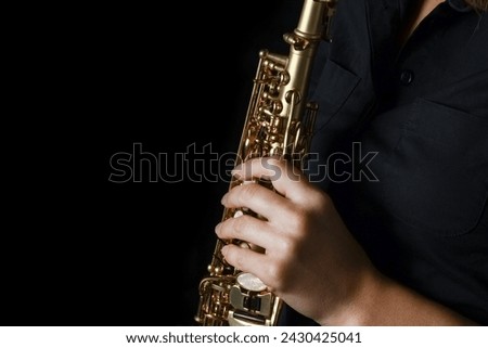 soprano saxophone in hands on a black background Royalty-Free Stock Photo #2430425041