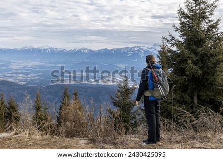 A tourist with a backpack and hiking poles in Austria, looking at the Karawanken alpine ridge Royalty-Free Stock Photo #2430425095