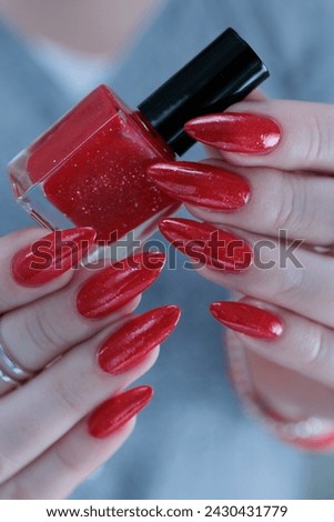 Female hand with long nails and a bottle of bright red nail polish