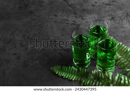 Absinthe in shot glasses and fern leaves on gray table, space for text. Alcoholic drink
