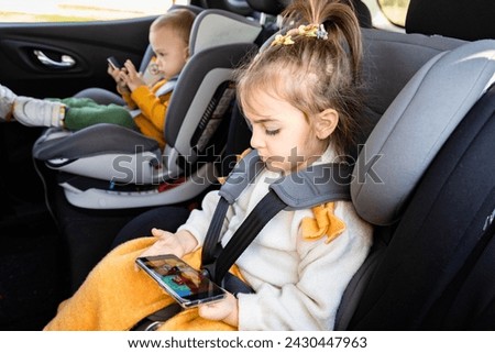 Side view of brother and sister on car back seat holding smart phones while traveling.