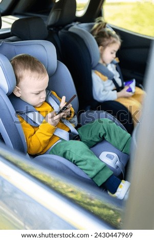 Brother and sister on car back seat holding smart phones while traveling.