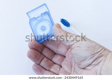 A hand holds dental floss for removing impurities between teeth, and in the background a sonic toothbrush, regular care of teeth and interdental spaces.