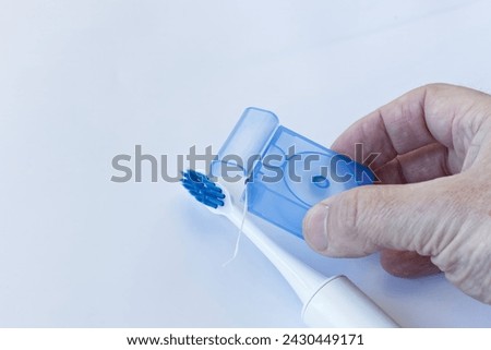 A hand holds dental floss for removing impurities between teeth, and in the background a sonic toothbrush, regular care of teeth and interdental spaces.