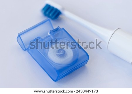 Floss to remove impurities between teeth, and consider a sonic toothbrush in the background, reminder to take regular care of your teeth and interdental spaces.