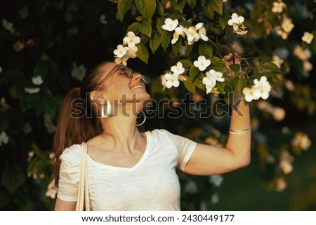 Summer time. happy modern female in white shirt with eyeglasses near flowering tree. Royalty-Free Stock Photo #2430449177