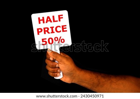 HALF PRICE notice board holding hand with black background close-up view, Human hand holding a white board with half price sale concept photography 