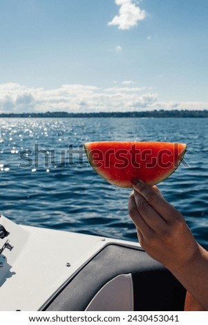 hand holding up watermelon semi circle, half moon with lake, sea, water background on sunny day Royalty-Free Stock Photo #2430453041