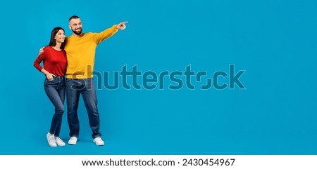 Check This. Happy Young Couple Pointing Aside At Copy Space, Smiling Millennial Man And Woman Showing Free Place For Your Advertisement Or Offer, Standing Together On Blue Background, Full Length Royalty-Free Stock Photo #2430454967
