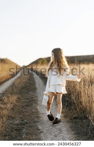 a lonely girl in light clothes with a small toy suitcase in the middle of an empty road in a field