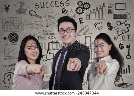 Portrait of multi ethnic business team pointing at camera in front of scribbles