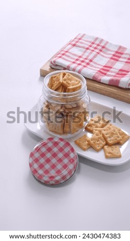 Small salty rectangular crackers in glass jar with white background

