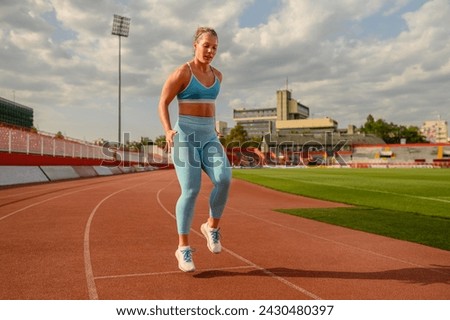 A fit female athlete in shape is running at stadium on running track. A sportswoman in motion running outdoors. A runner in action. A healthy sportswoman is practicing at stadium. Body conscious. Royalty-Free Stock Photo #2430480397