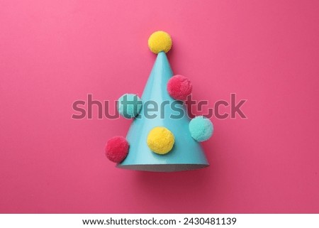 One light blue party hat with pompoms on pink background, top view