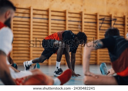 An african american professional basketball player is stretching leg on court during training with his teammates. Multicultural basketball team is warming up before training on basketball court.