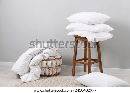 Soft pillows, duvet and chair near light grey wall indoors Royalty-Free Stock Photo #2430482977