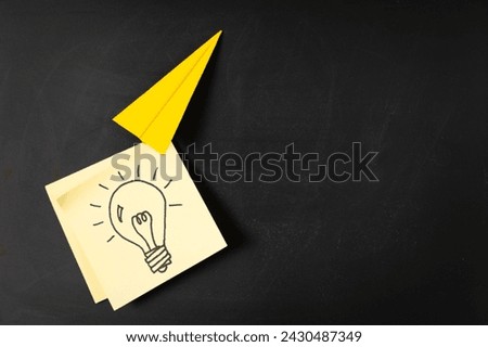 Origami paper airplane carries a hand drawn light bulb symbol on yellow sticky note paper, concepts of new, unique, creative or innovative idea in business success, marketing growth