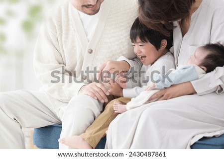 A Japanese couple holds their small children by the window of their living room, which is bathed in bright sunlight. Close-up photo of the children with no parent's faces in the picture.