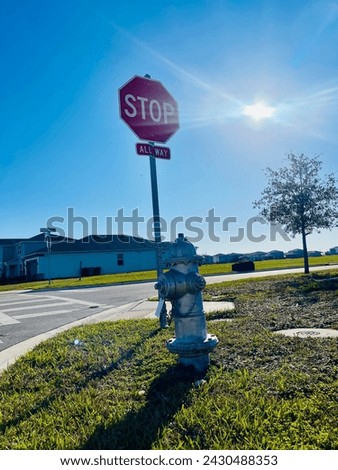 Traffic sign with a stop sign and a fire hydrant in the middle of a green field in the afternoon