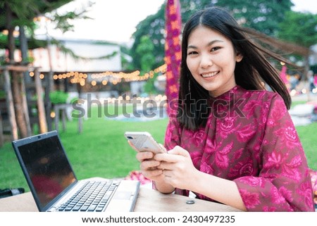 Beautiful asian business women use smartphone text message sitting on grass in party park outdoor background