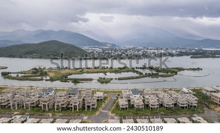 Aerial view of an unfinished housing development with lake and mountain scenery in the background, under overcast skies perfect for real estate and urban planning concepts Royalty-Free Stock Photo #2430510189