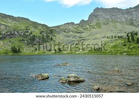 Flat stones sticking out of a lake above the surface of the water, surrounded by high mountain ranges on a cloudy summer day. Marble Lake, Ergaki Natural Park, Krasnoyarsk Territory, Siberia, Russia.