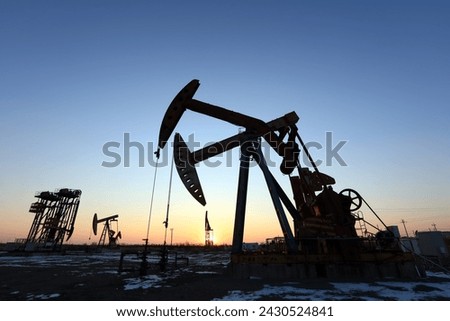 Oil field site, in the evening, oil pumps are running, Silhouette of beam pumping unit Royalty-Free Stock Photo #2430524841
