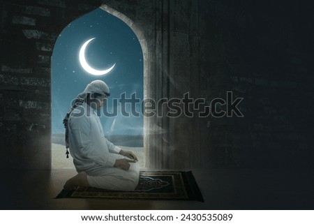 A Muslim man with agal in a praying position (salat) in the mosque with a night scene view background. Muslim concept Royalty-Free Stock Photo #2430535089