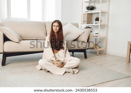 Cozy Morning Bliss: Smiling Woman Holding Coffee Mug in Warm Autumn Home, Wrapped in a Blanket on Sofa