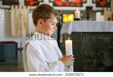 Little kid boy receiving his first holy communion. Happy child holding Christening candle. Tradition in catholic curch. Kid in a white traditional gown in a church near altar. Royalty-Free Stock Photo #2430570271
