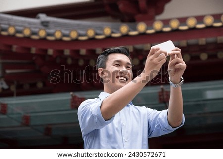 Happy Asian man on holiday using his digital tablet to take a photo. Chinese temple in the background.