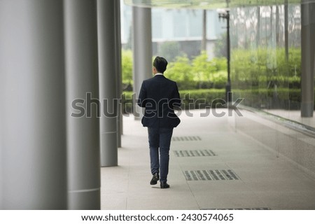 Back view of an Asian businessman walking away from camera in the city. Royalty-Free Stock Photo #2430574065
