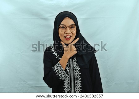Asian Muslim woman wearing hijab, glasses and black dress with white pattern making chis gesture with a satisfied expression isolated on white background Royalty-Free Stock Photo #2430582357
