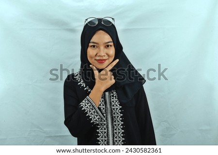 Asian Muslim woman wearing hijab, glasses and black dress with white pattern making chis gesture with a satisfied expression isolated on white background Royalty-Free Stock Photo #2430582361
